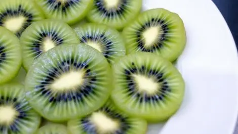 Realistic close up photo of fresh sliced kiwifruit on white plate